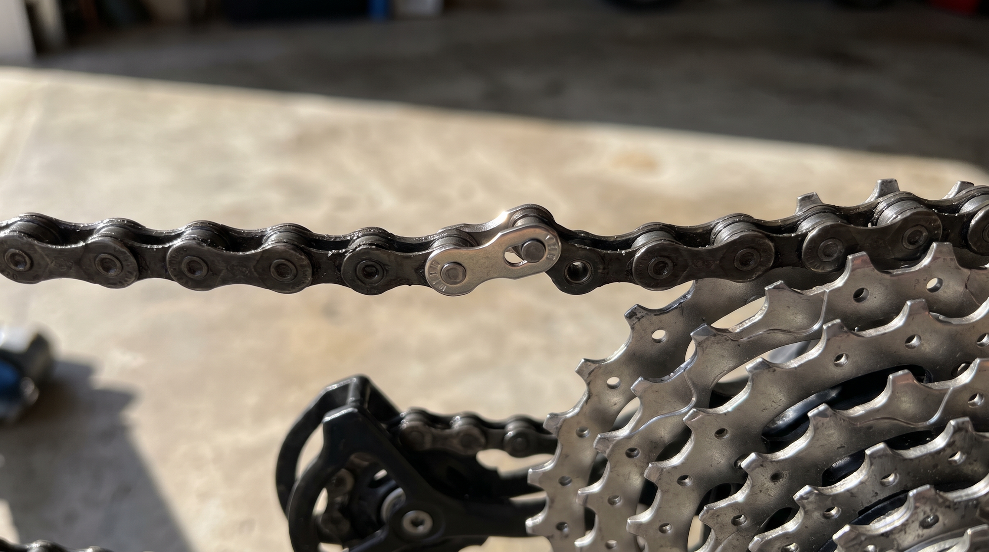 Fahrradkette mit silbernem Kettenschloss über Kassette und Schaltwerk im Makro, Kettenschloss nach der Montage prüfen